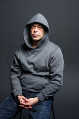 Naklejka na ściany i meble Studio portrait of a 40-50-year-old serious man in a gray hoodie on a neutral background, eyes directed at the camera, swollen eyes. Maybe he's an actor or a truck driver, a lawyer or a retired milita