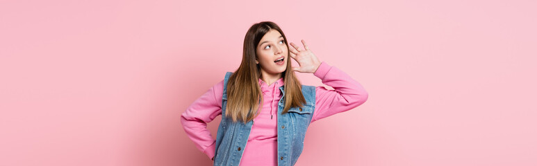 Teenager with hand near ear looking away on pink background, banner