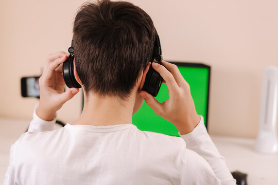 Process of teenage boy puts on headphones befour starting play games. Side view of boy preparing for gaming. Green screen