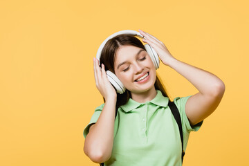 Cheerful teen girl listening music in headphones isolated on yellow