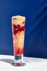 Raspberry and banana smoothie over white and blue background. Palm leaf with sunshine and hard shadow. Fruit yogurt or shake drink in high glass. Summer, healthy, fresh drink concept