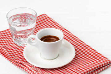 Cup of espresso with glass of water on white table