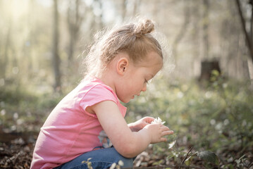 Beautiful happy cute young girl picking wild flowers crouching down on summer day in woods peaceful...