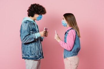 Side view of teenagers in medical masks showing digital tablets on pink background