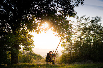 A wide shot of a girl drawing in nature under the sunset. A young artist uses an easel under a tree to draw nature