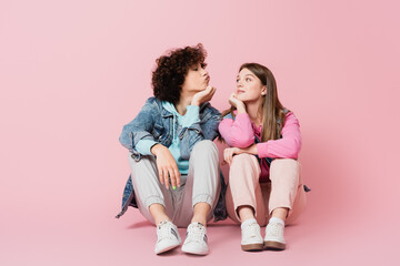 Curly teenager pouting lips near girlfriend on pink background