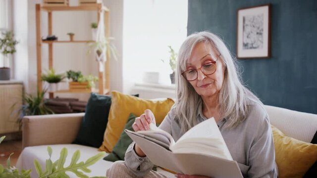 Portrait of senior woman sitting indoors on sofa at home, reading book.