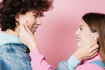 Side view of smiling teenager holding earphones on pink background