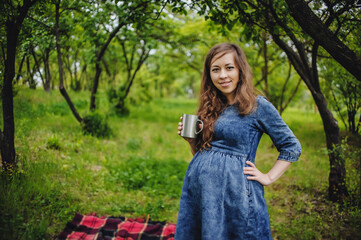 Expectation of the child. A pregnant woman in the dress, with long hair in the park, a garden with a mug of hot tea. Nine months. concept of motherhood, the birth of a child. Happy mama