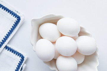 White eggs in a white dish and napkins on the table on a light background. Easter card, top view