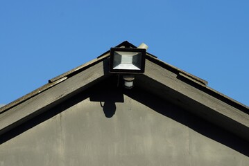 one square led white black lantern hanging on a plank of a concrete loft against a blue sky