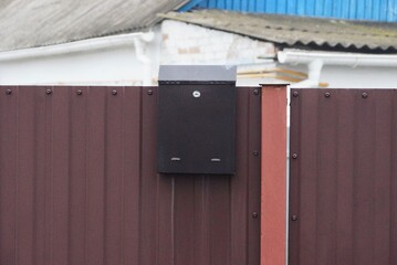 one iron brown mailbox hanging on a metal fence wall in the street