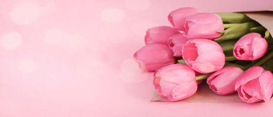 Fototapeta premium Bouquet of tulips wrapped in craft paper on pink background with space for text. Greeting card. Concept woman's or mother's day. Spring flowers background. Banner