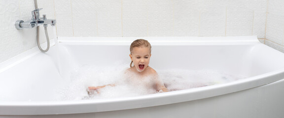 Small cute caucasian child sitting at bath, washing, playing with soap and foam, emotions at little face, indoor, copy space, white background, happy childhood, banner.