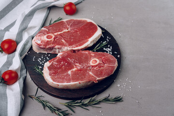 Raw rib-eye beef steak on wooden cutting board on gray background