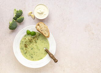 Broccoli cream soup served with cream and fresh bread on light concrete background. Healthy vegetarian food concept.