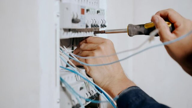 An electrician assembles an electrical panel in an apartment. Electrical box contains many terminals, relays, wires and switches. Manufacture and installation concept concept.