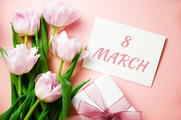 Banner. A bunch of pink tulips on a warm pink background with a card with 8 march text and a gift. Flatlay