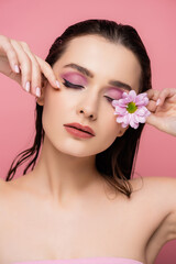 Fototapeta na wymiar sensual young woman with closed eyes holding flower isolated on pink