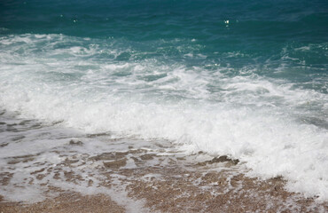 Blue wave with white foam on a sunny beach, relaxation by the sea, relaxation