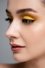 Fototapeta premium close up of young woman with yellow eyeshadow looking away isolated on grey