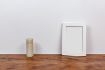 Minimalist still life of a customizable picture frame and prehistoric cylindrical idol. Wood and white background.