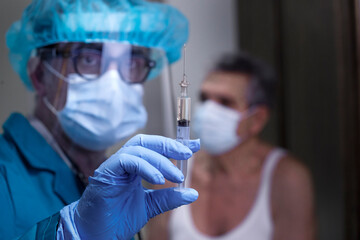 Dottore con tutte le protezioni mediche prepara una siringa con il vaccino per un anziano signore...