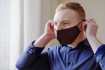A young man puts on a protective mask on his face as protection against coronavirus - A mask on a...