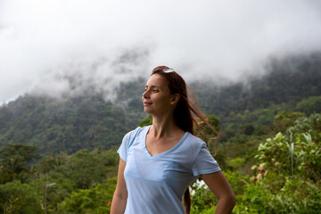 Naklejka premium Happy woman portrait in mountain landscape with white clouds. Candid face portrait on top of mountain. Female tourist in natural environment. Hiking and trekking concept. Cloudy forest landscape
