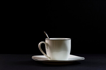 Porcelain spoon, cup and plate on black background. The photograph is a horizontal shot taken in a studio under artificial lighting.