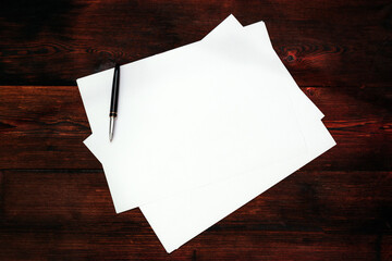Blank sheet of paper with a pen on a dark wooden background. Letter concept. The beginning of the...
