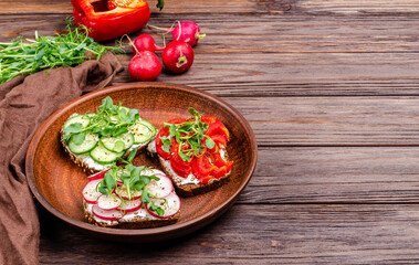 Different sandwiches with cucumber, radish, red paprika and microgreens on a plate on a wooden background.