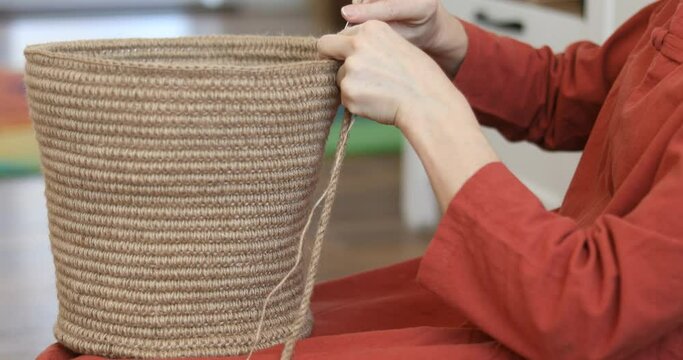 The woman is crocheting from environmentally friendly materials. Jute fiber for home decor. Home hobby of weaving thick-walled rope baskets. Handwork in the interior. Knitted jute and rope baskets.