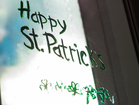 Drawing St. Patrick's Day painting green three-leaved shamrocks indoor, festive home decoration, quarantine family leisure. Child draws clovers and hearts on window glass. Stay home concept New normal
