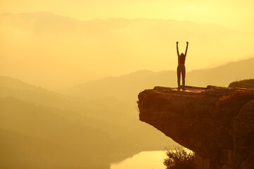 Woman silhouette celebrating in the top of a cliff - obrazy, fototapety, plakaty