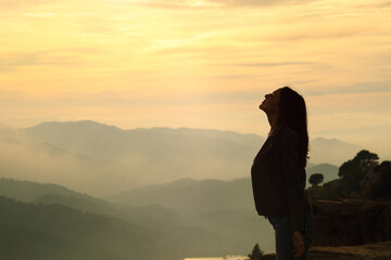 Woman silhouette breathing fresh air in the mountain at sunset