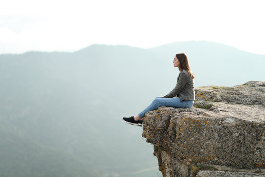 Woman contemplating views on the top of a cliff in the mountain