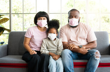 Mixed Race family sitting on the sofa and wearing medical face masks for against coronavirus world pandemic and stay quarantined together at home social distancing new normal lifestyle