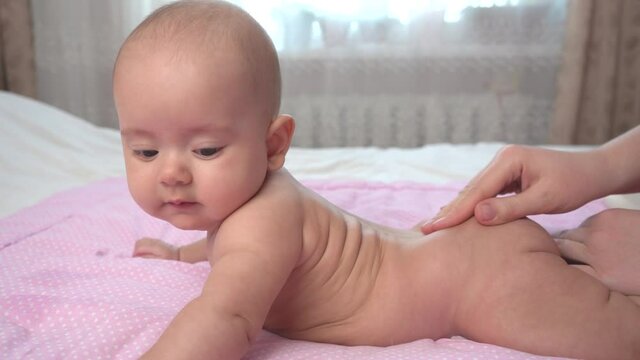 Mom makes a back massage to the newborn lying on the bed. Happy child