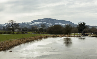 Frozen canal with fields and hills in winter