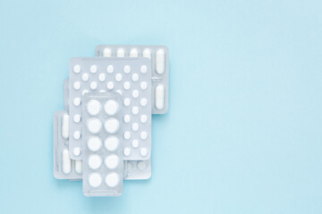 Blisters of white pills on blue background, top view. Various pharmaceuticals, tablets, medicine capsules. Treatment concept. Copy space.