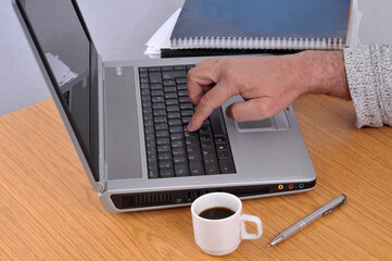 Quelqu'un travaillant sur un ordinateur portable à côté d'une tasse de café et de documents papier