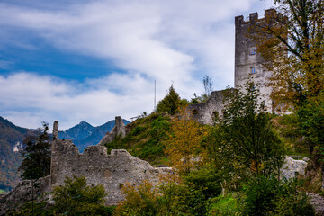A dilapidated ruin of an old knight's castle, overgrown with green trees and bushes, and damaged - taken on a cloudy summer's day in the mountains of the Bavarian Alps