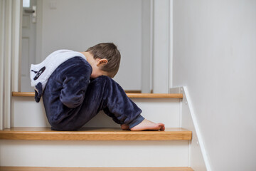 the unhappy child is sitting on the stairs with his head down