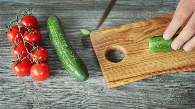 very close up view male hands cutting cucmber with kitchen knife on wooden chopping board
