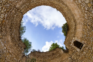 Tall stone walls form a perfect circle in the sky. Old well to conserve snow. Low Angle view. La Cava de Don Miquel