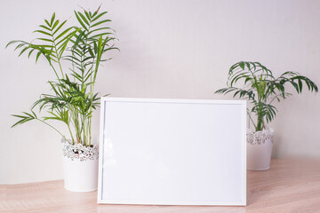 Portrait white picture frame mockup on wooden table. Modern  vases with palms. White wall background. Scandinavian interior. 