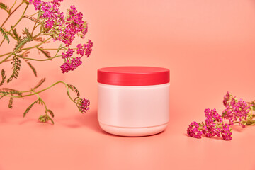pink jar without inscriptions. against the background of red flower yarrow. concept cosmetics skin care