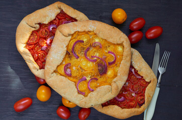 Tomato galette with onion rings on the black wooden background decorated with various cherry tomatoes. Traditional Italian vegetarian food. Top view