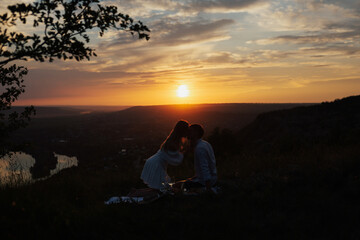 Fototapeta na wymiar Silhouette of sensual young couple in love kissing at the summer picnic at amazing sunset.